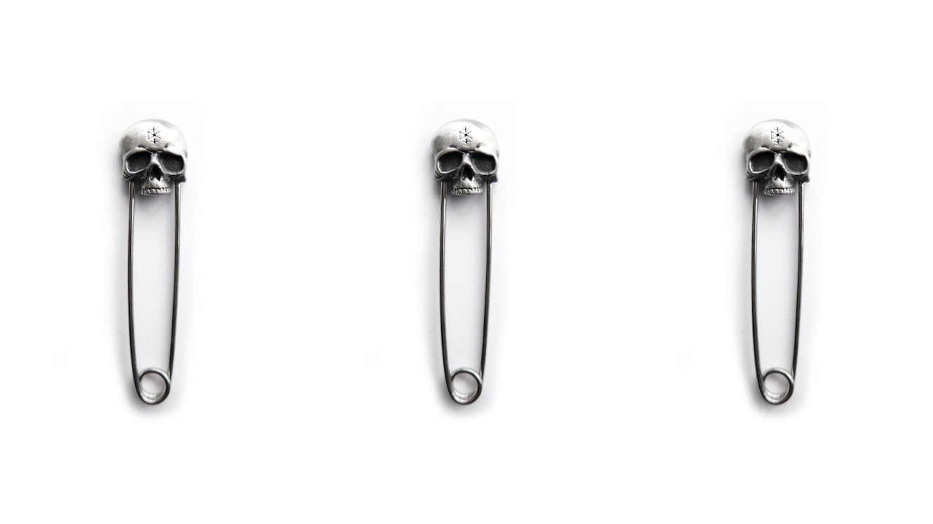 Silver safety-pin brooch topped with a small skull